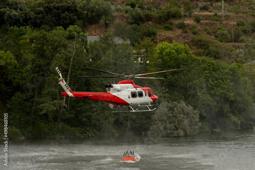 A helicopter pilot scoops up water with a bucket from a river to blow off the mountain