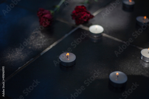 Candles on gravestone. Wax candles burn on war monument. Two flowers on tombstone. Burial place of soldiers.