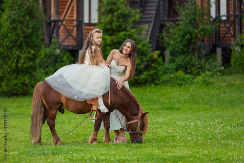 mother rides her daughter on a pony on a green lawn © zokov_111