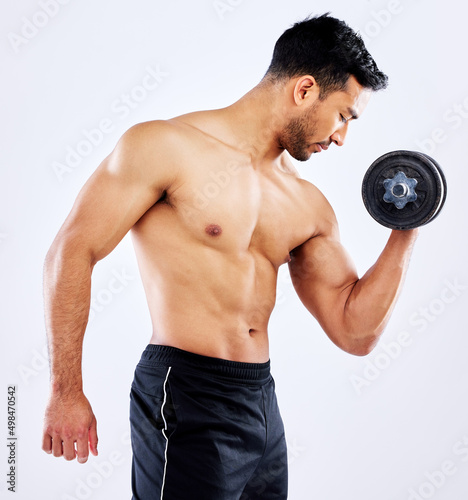 Think about the bigger picture. Shot of a young man flexing his bicep muscles while holding a weight against a studio background.