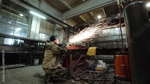 Heavy Industry Engineering Factory Interior with Industrial Worker Using Angle Grinder and Cutting a Metal Tube. Contractor in Safety Uniform and Hard Hat Manufacturing Metal Structures. a worker with