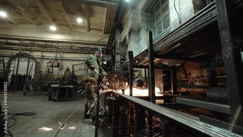 Heavy Industry Engineering Factory Interior with Industrial Worker Using Angle Grinder and Cutting a Metal Tube. Contractor in Safety Uniform and Hard Hat Manufacturing Metal Structures. a worker with