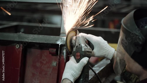 Heavy Industry Engineering Factory Interior with Industrial Worker Using Angle Grinder and Cutting a Metal Tube. Contractor in Safety Uniform and Hard Hat Manufacturing Metal Structures. a worker with