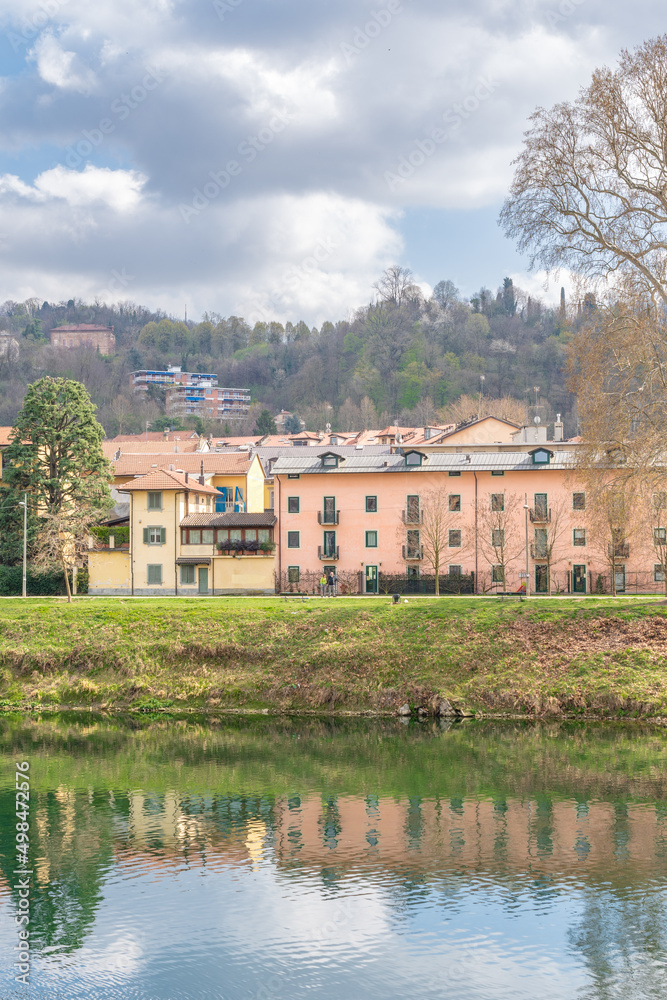 Colored European houses facing the river. Landscape with a forest behind and reflection of the houses in the river. A sky with clouds. Colored European houses facing the river. Landscape with a forest behind and reflection of the houses in the river. A sky with clouds.