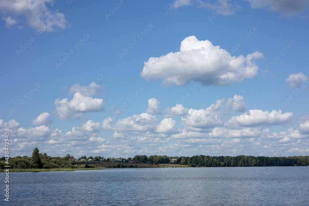 Summer countryside landscape with blue sky and calm water of river.