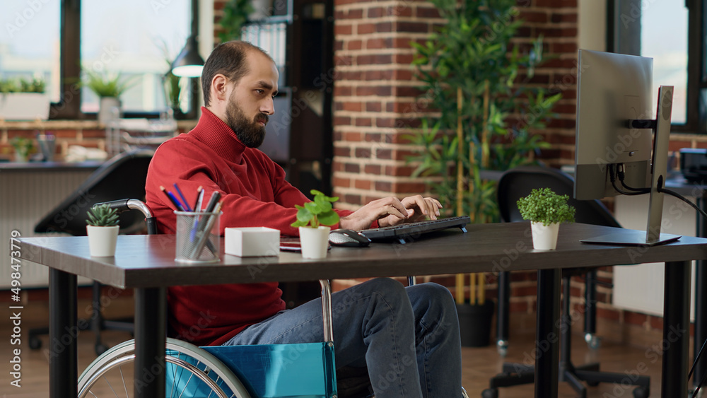 Manager with impairment working on business growth with computer at desk, witting in wheelchair. Male worker planning financial strategy to create executive company development. Manager with impairment working on business growth with computer at desk, witting in wheelchair. Male worker planning financial strategy to create executive company development.