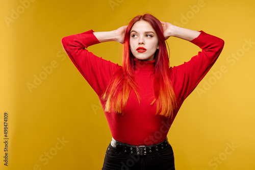 Young pretty woman with red hair and red sweter posing on yellow background