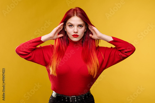 Young pretty woman with red hair and red sweter posing on yellow background