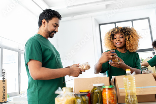 charity  donation and volunteering concept - international group of happy smiling volunteers packing food in boxes at distribution or refugee assistance center