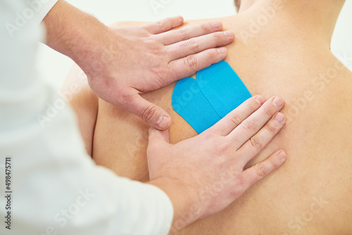 kinesiology therapeutic strip tape applying on male back for pain relief photo