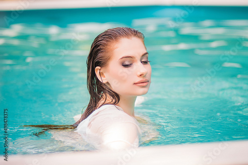 Portrait of a beautiful girl with wet hair floating in the pool  wearing a white shirt. Rest in the water in hot weather. 