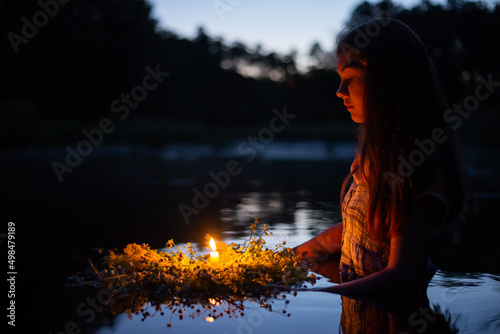 Portrait of a small girl in river late at night, set the wreath to float with a candle. Ivan Kupala tradition in Ukraine photo