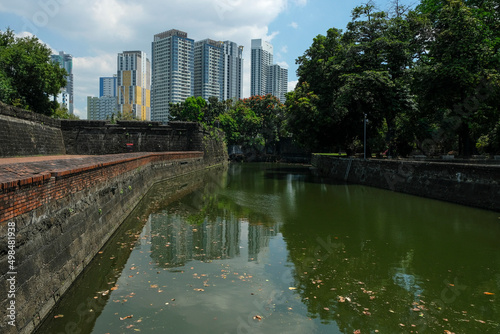 Views of the Fort Santiago moat with Manila's skyscrapers in the background. Intramuros in Manila, Philippines. The defense fortress is located in Intramuros, the walled city of Manila.