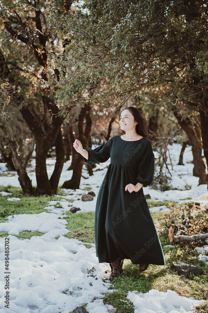 Happy smiling Girl in a rustic style green dress dancing in the olive grove early spring with snow and green grass simultaneously Happy smiling Girl in a rustic style green dress dancing in the olive grove early spring with snow and green grass simultaneously