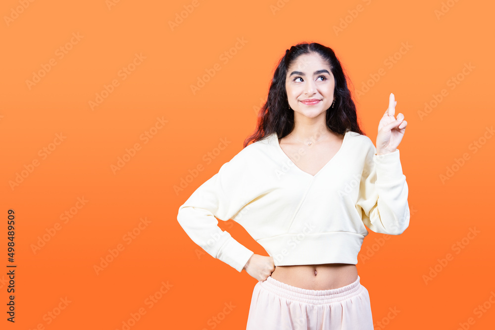 Young woman crosses her fingers for good luck. She wants the dream to come true. Orange background with copy space.
