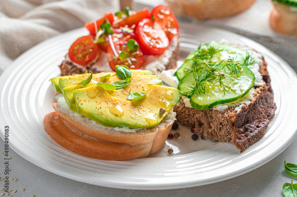 Three sandwiches with feta cheese, avocado, cherry tomatoes and cucumber in a white plate.