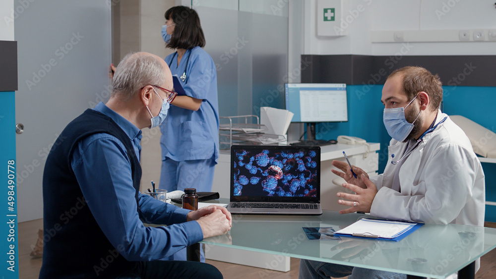 Physician explaining coronavirus spreading with illustration on laptop, giving medical advice to elder man at checkup visit. Medic and patient looking at virus animation on display.