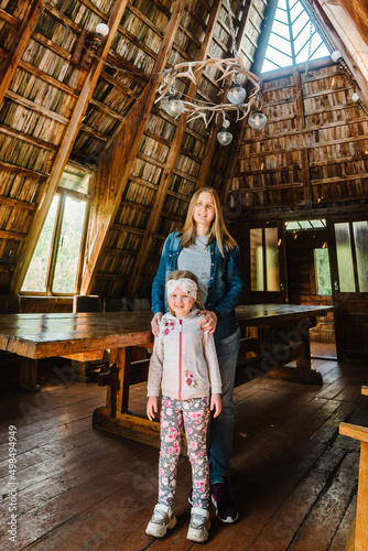 Young mother and daughter standing in an old wooden house. Happy mother hugs the girl. Old wooden architectural house.