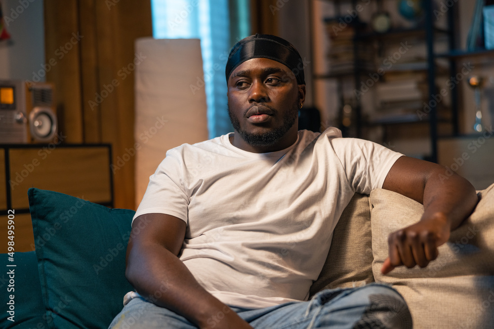 A bored guy is relaxing on the living room sofa in front of the television. The young man stares at a weak movie, TV series, comedies, losing soccer game. A bored guy is relaxing on the living room sofa in front of the television. The young man stares at a weak movie, TV series, comedies, losing soccer game.