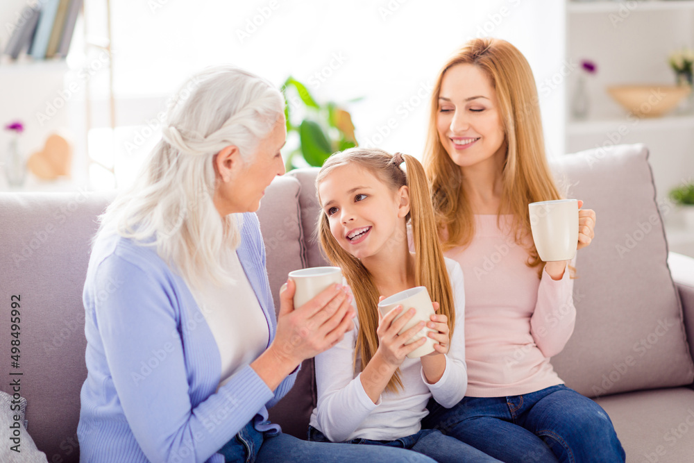 Photo of three cheerful idyllic people sitting couch hold drink mug communicate house indoors