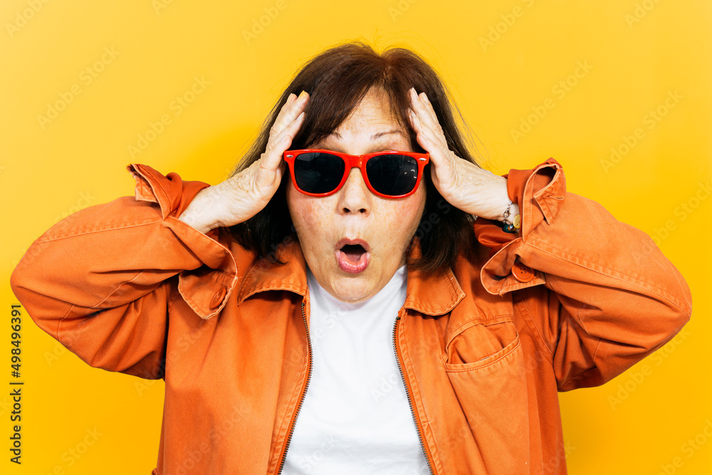 Amazed woman with red sunglasses and orange jacket on yellow colored background. Amazed woman with red sunglasses and orange jacket on yellow colored background.
