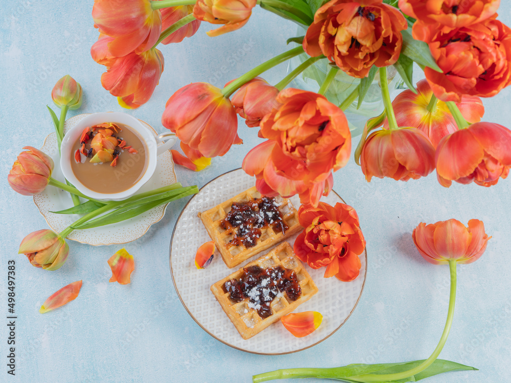 Fototapeta premium Scarlet, red tulips in a vase and a white cup with coffee and French waffles. The concept of congratulations and old holidays. There is a place for text.