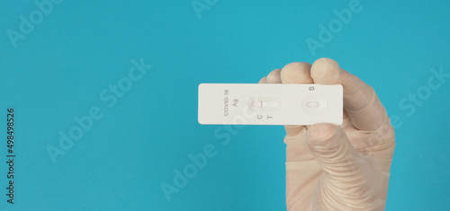 A hand hold ATK ( antigen test kit) and wear medical glove on blue background.