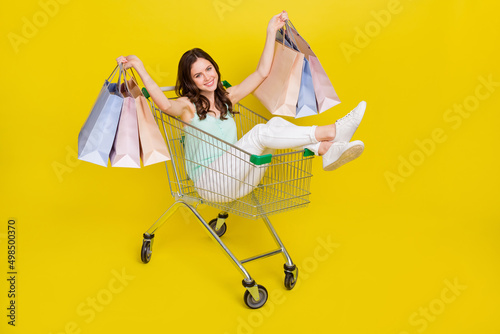 Full size photo of excited crazy person sit trolley hold packages isolated on yellow color background