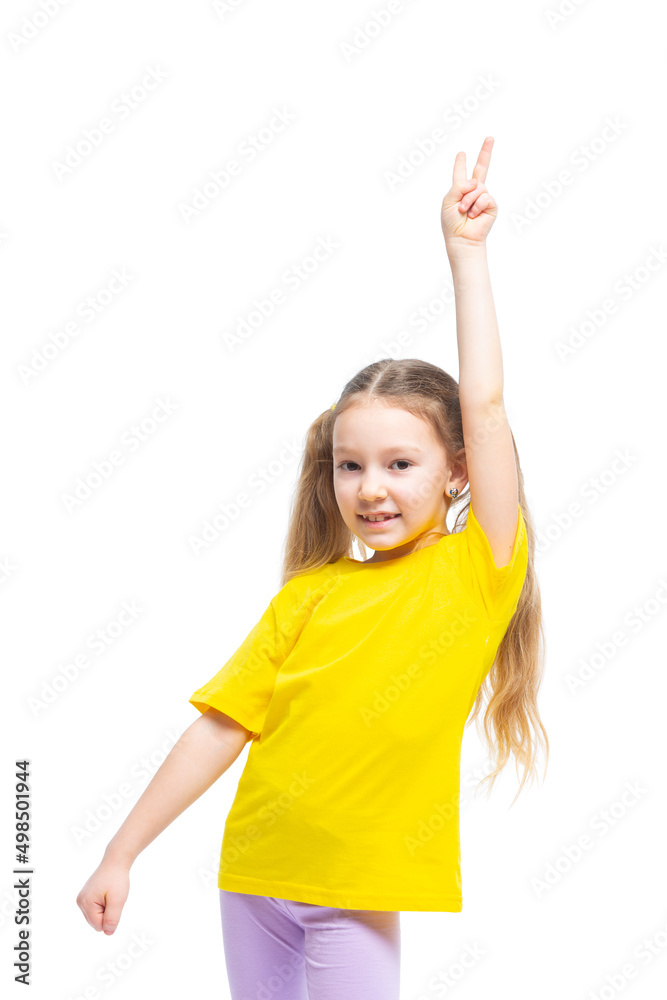 Happy and cheerful child shows victory gesture. The girl is wearing a yellow t-shirt and purple pants. Happy and cheerful child shows victory gesture. The girl is wearing a yellow t-shirt and purple pants.