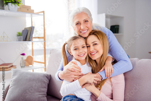 Portrait of three peaceful positive people cuddle sitting sofa toothy smile look camera house indoors