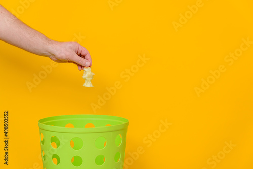 A man's hand throws an apple core into a trash can, yellow background, space for text.