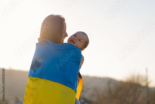 Valokuva Woman hugs her little son wrapped in yellow and blue flag of Ukraine in outdoors
