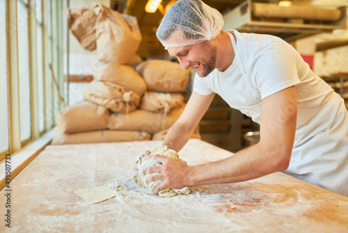 Young man as a baker in training kneading the dough photo