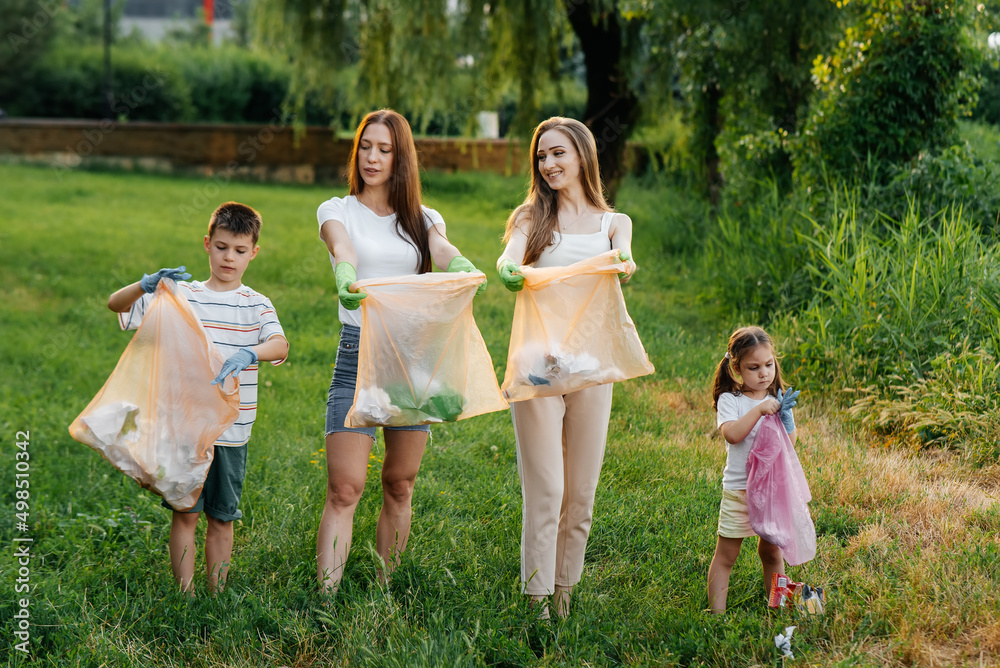 Naklejka premium A group of adults and children together at sunset is engaged in garbage collection in the park. Environmental care, waste recycling. Sorting garbage.