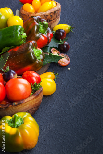 Assorted tomatoes and vegetables on dark background. Photo for your design.