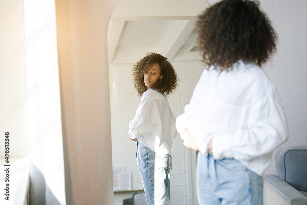 Fototapeta premium Cute african american girl choosing clothes to wear in front of mirror in i the living room. Morning wake up concept 
