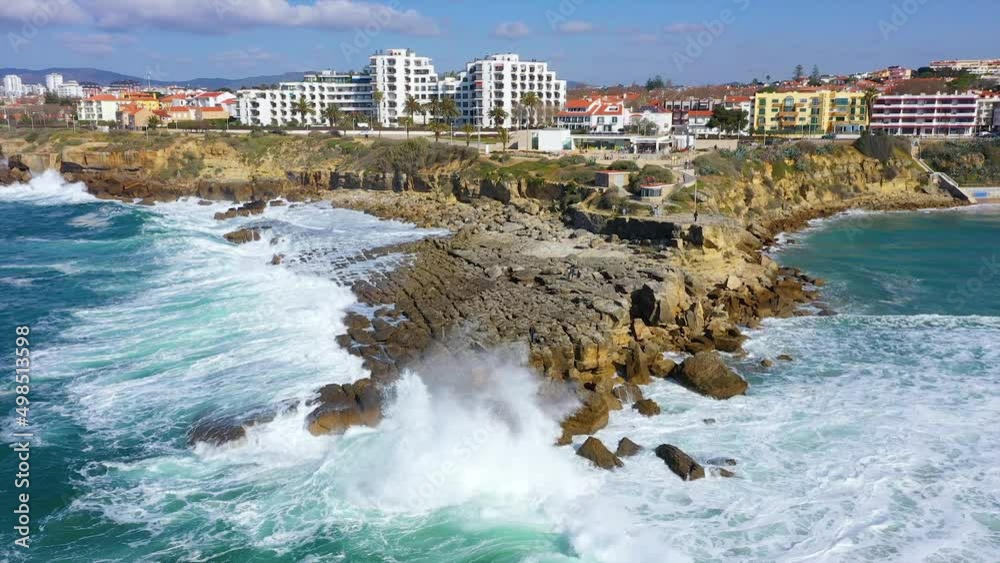 Aerial view of waves hitting the rocky coastline of Miradouro Pedra do Sal, in Lisbon, sunny Portugal - circling, drone shot