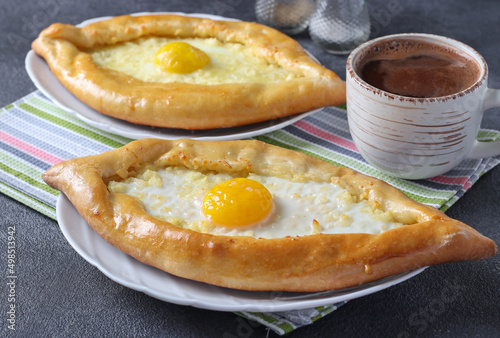 Khachapuri in Adjarian, Open pies with suluguni cheese and egg yolk in the form of a boat on plates on gray background, Traditional Georgian cuisine