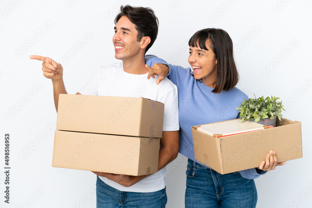 Young couple making a move while picking up a box full of things isolated on white background pointing to the side to present a product Young couple making a move while picking up a box full of things isolated on white background pointing to the side to present a product