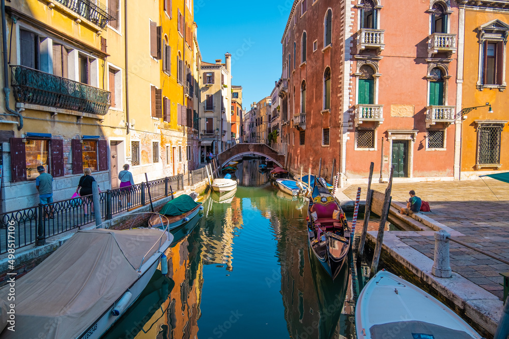 View of empty gondola on narrow canals, with a tourist waiting for the gondolier of Venice, Italy.