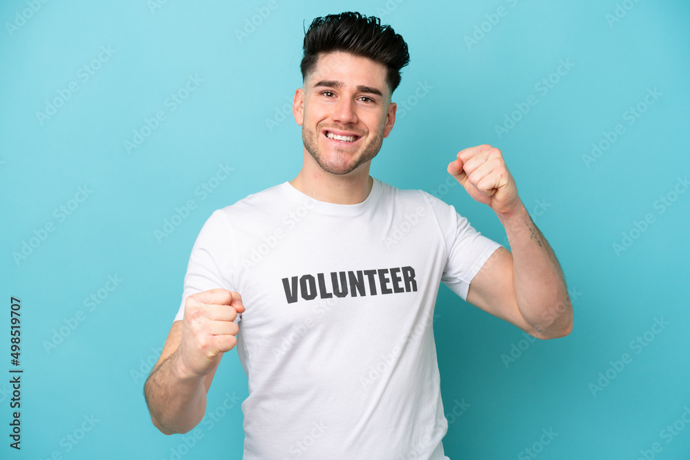 Young volunteer caucasian man isolated on blue background celebrating a victory Young volunteer caucasian man isolated on blue background celebrating a victory