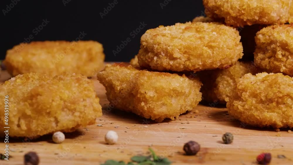 Close up of vegan chicken nuggets on a cutting board with some basil leaf and peppercorn garnish rotate against a black background Close up of vegan chicken nuggets on a cutting board with some basil leaf and peppercorn garnish rotate against a black background