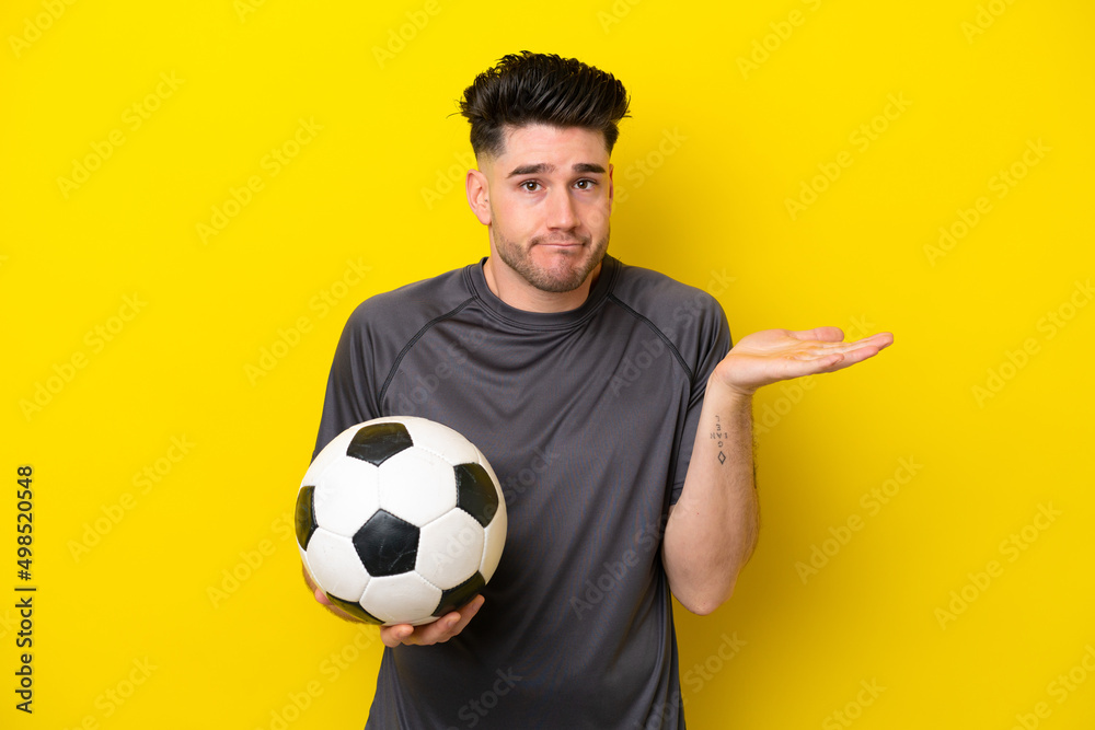 Handsome young football player man isolated on yellow background having doubts while raising hands