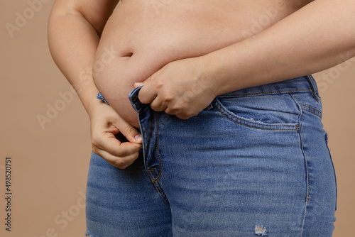 Overweighted lady with large abdomen in process of zipping up blue jeans. Sudden weight gain. Visceral fat. Body positive. Tight little clothes. Need for wardrobe change.