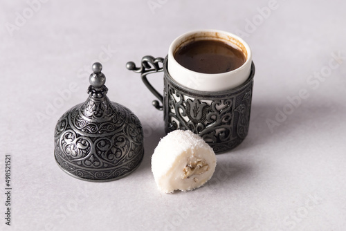 Pouring Turkish Coffee into Traditional Embossed Metal Cup and Coconut Lokum Gray Background photo