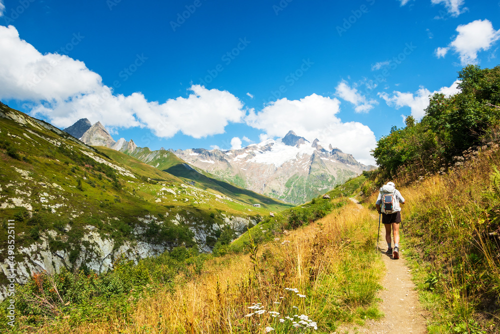 Senior man hiking French Alps in summer with solar backpack. The Aiguille des Glaciers, mountain in the Mont Blanc massif. View From Chapieux valley, Savoie, France.