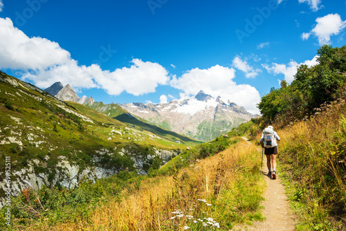 Senior man hiking French Alps in summer with solar backpack. The Aiguille des Glaciers, mountain in the Mont Blanc massif. View From Chapieux valley, Savoie, France.