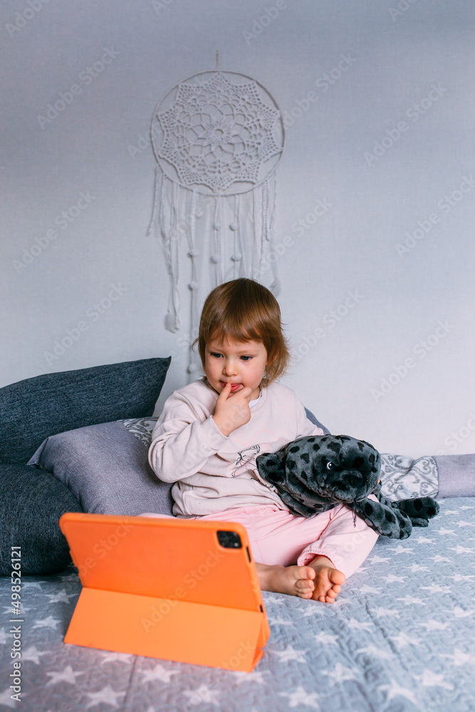 Naklejka premium Small child watches cartoons at home on sofa on the tablet. Kid use technology