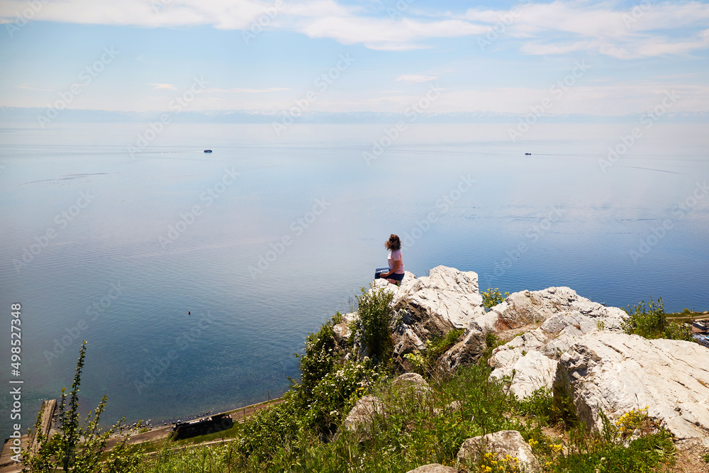 A woman is sitting at the cliff and enjoying a beautiful view of the port of Baikal. Lake Baikal in summer.