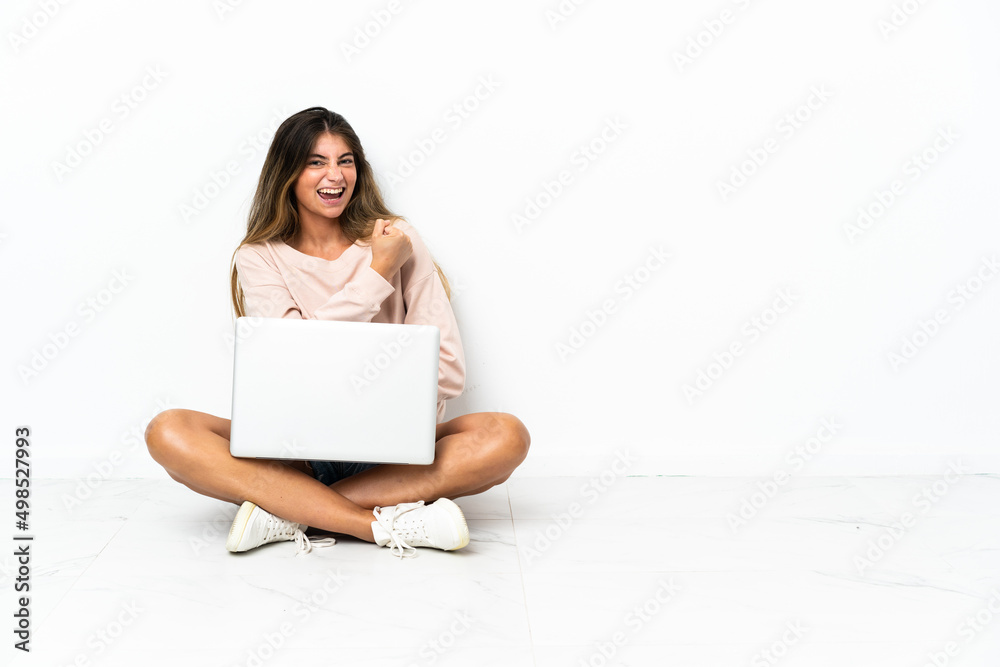 Young woman with a laptop sitting on the floor isolated on white background celebrating a victory Young woman with a laptop sitting on the floor isolated on white background celebrating a victory